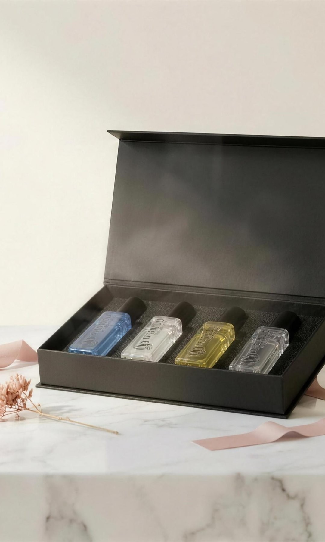 The Descent Discovery Gift Set open on a marble plinth — four 20ml bottles in a matte black magnetic box with a blush ribbon